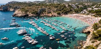 Una baia del Mediterraneo completamente invasa da imbarcazioni ancorate vicino alla costa.